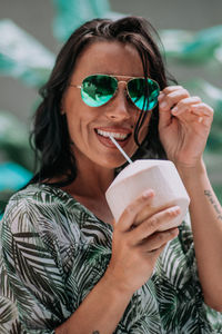 Portrait of a smiling young woman holding sunglasses