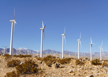 Wind turbines in the desert with a mountain backdrop.