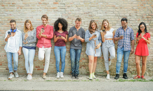 Full length of friends using phone while standing outdoors