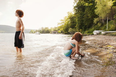 Girl playing at shore while brother standing in lake