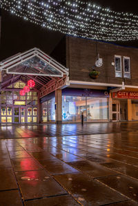 Illuminated wet street by buildings in city at night