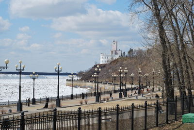 View of city at riverbank against cloudy sky