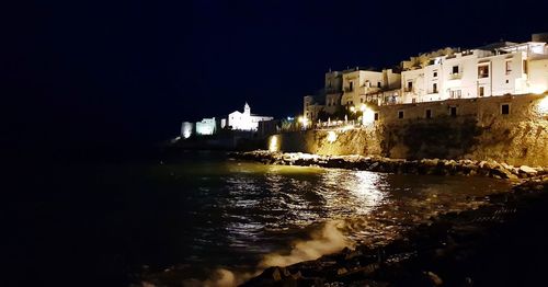 Illuminated buildings by sea against clear sky at night