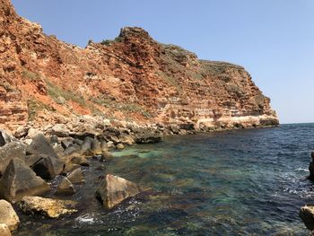 Rock formations by sea against clear sky