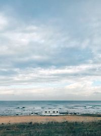 Camper van on shore at beach against cloudy sky