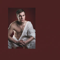 Portrait of young man sitting against wall