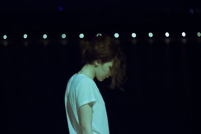 Girl looking down while standing outdoors at night