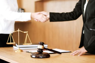 Midsection of lawyer shaking hand with client at office