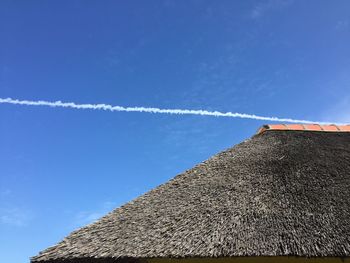 Low angle view of thatched roof and vapor trail against blue sky