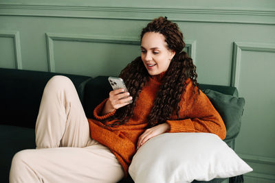 Young woman using mobile phone while sitting on sofa at home