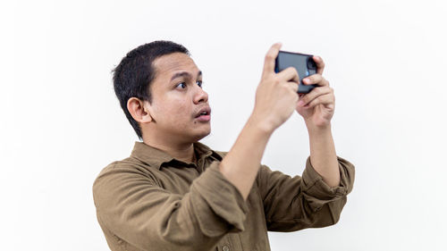 Portrait of young man photographing against white background