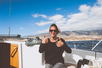 Woman with sunglasses on boat showing thumbs up sign against sky