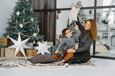 Mother with child playing near christmas tree. child unpacking gifts, parent enjoy christmas tree