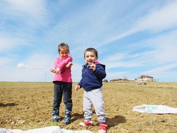 Portrait of happy siblings playing on field against sky