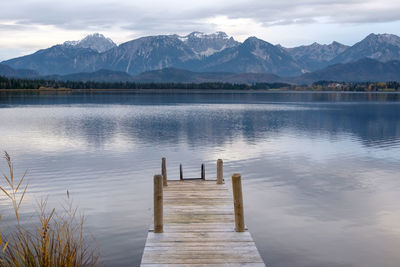 Wooden posts in lake by mountains against sky