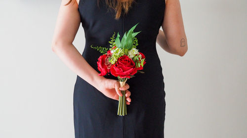 Midsection of woman holding red rose against white background