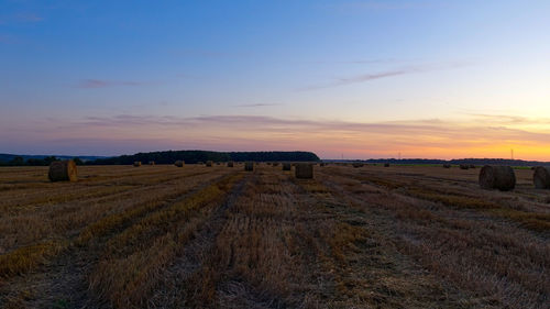 Hay bales on field against sky during sunset