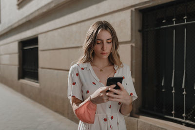 Young woman using mobile phone while standing on wall