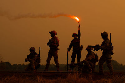 Armed forces standing on railroad track against sky during sunset