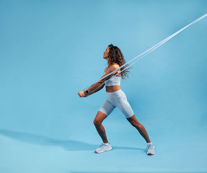 Full length of woman exercising against blue background