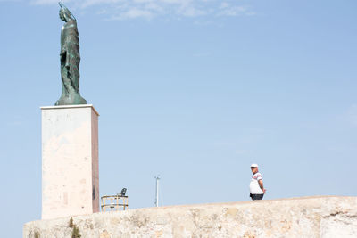 Low angle view of man standing on sculpture against sky
