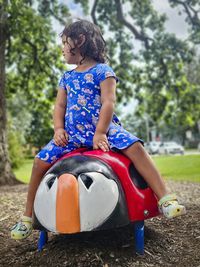 A young preschool girl rides a playground ladybug as she contemplates what is going on around her.