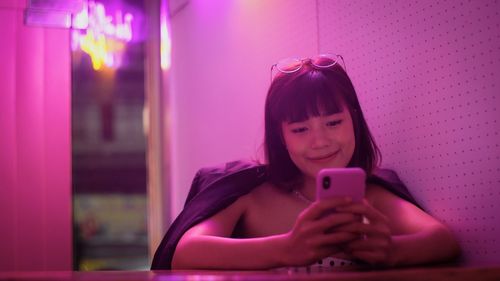 Smiling woman using mobile phone in illuminated room