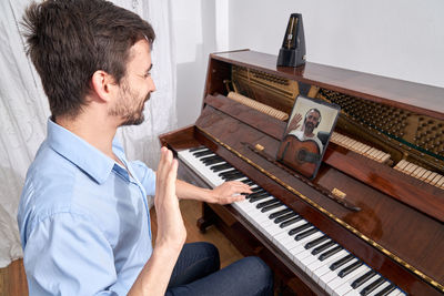 Side view of focused male musician playing piano while practicing from tablet