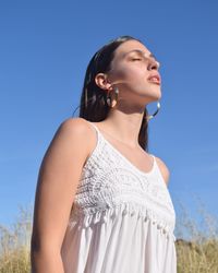 Low angle view of young woman standing on field against clear blue sky