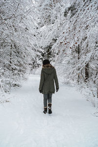 Rear view of woman walking amidst trees during winter