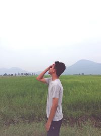 Side view of teenage boy standing on grassy landscape