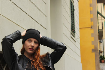 Portrait of young woman wearing hat standing against wall