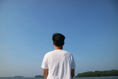 Rear view of man standing against clear blue sky