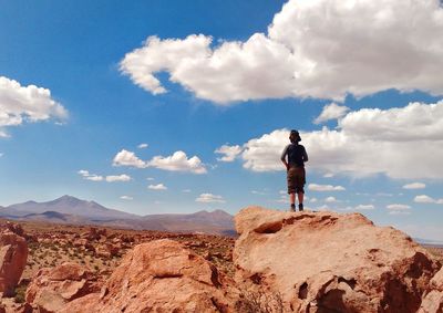 Man standing on rock looking at mountains against sky