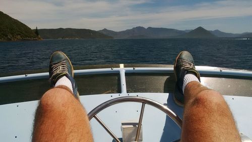 Low section of man on boat sailing in sea against sky