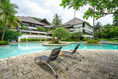 Chairs by swimming pool by building against sky