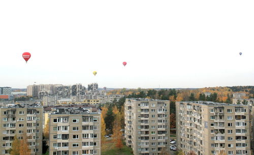 Hot air balloon flying over buildings in city against clear sky