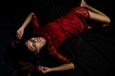 High angle view of beautiful woman wearing red dress while lying on bed at home
