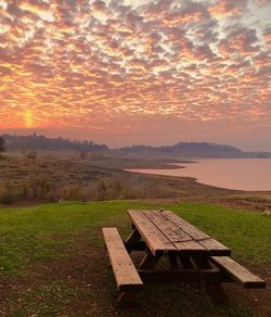 Bench on field against sky during sunset