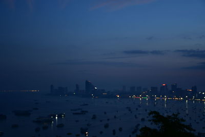 Illuminated city by sea against sky at dusk