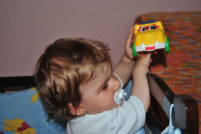 Cute baby boy sucking pacifier while playing with toy car at home