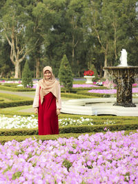 Woman standing by flowering plants against trees