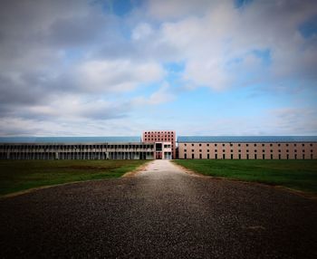 Road by building against cloudy sky