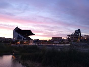 Bridge over river by buildings against sky at sunset