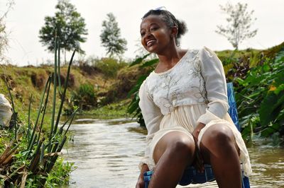 Young woman sitting on chair against stream against sky