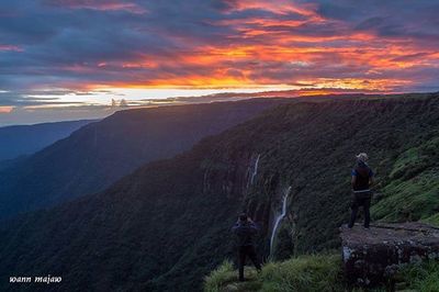 People standing on mountain against cloudy sky