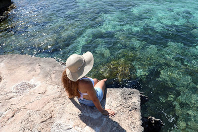 High angle view of woman sitting on rock at sea shore