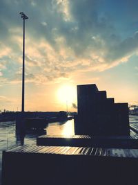 Silhouette buildings by sea against sky during sunset