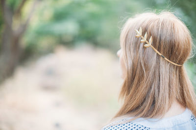Rear view of woman wearing brooch in long blond hair at forest