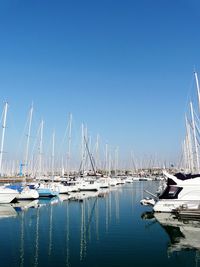 Sailboats moored in harbor against clear blue sky